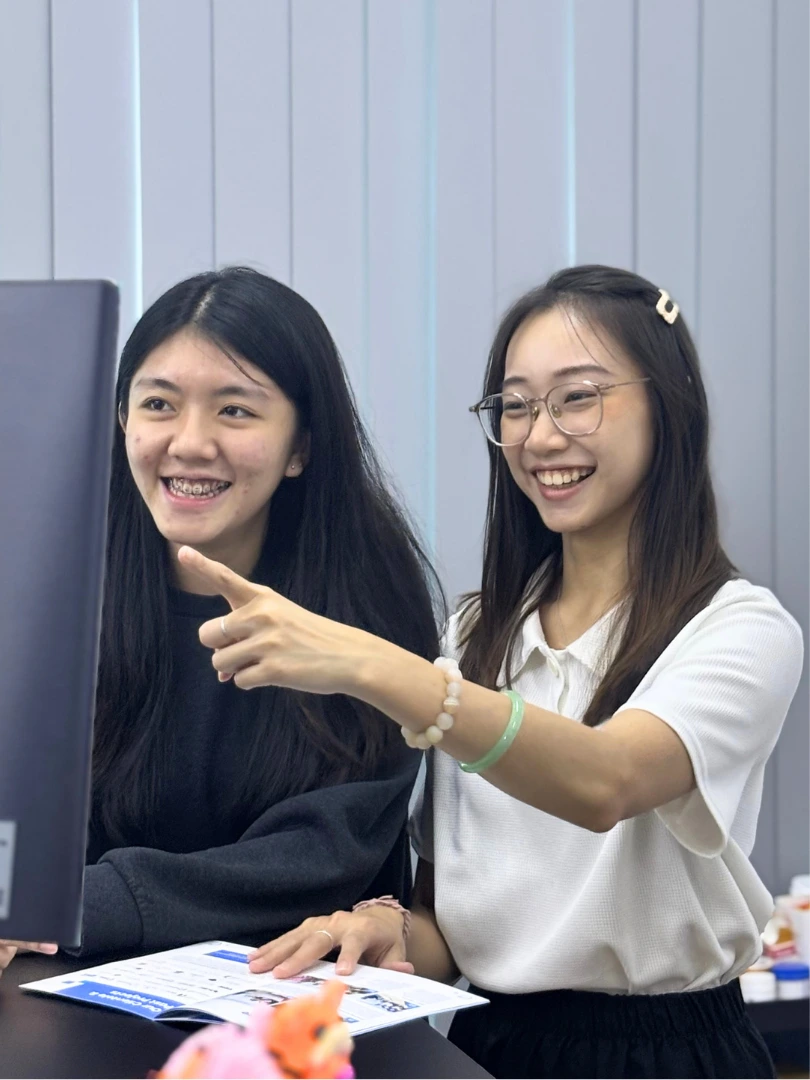 Two Plixitt team members smiling at a desk while reviewing work on a monitor